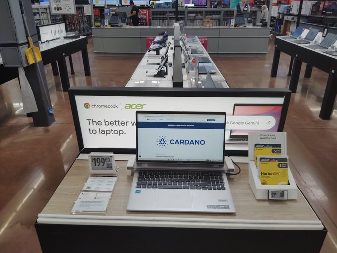 A display table in an electronics store featuring an Acer Chromebook Plus laptop priced at $199.99, with a 'CARDANO' logo prominently displayed on the screen.