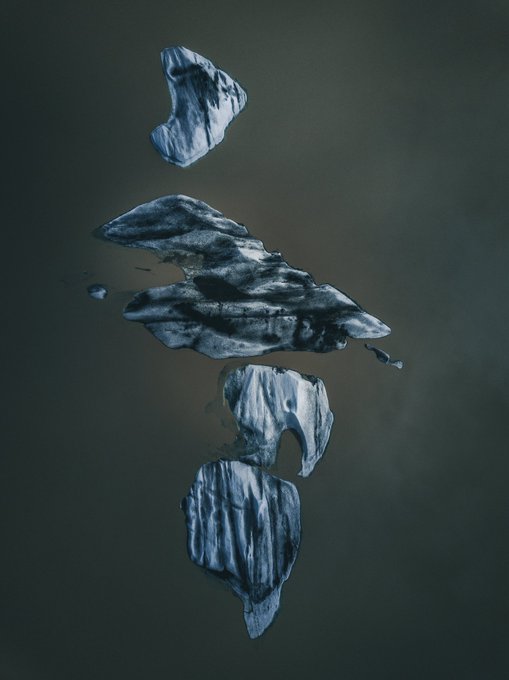 An abstract dark artwork depicts fragmented metallic or stone-like shapes arranged vertically against a moody gray background.