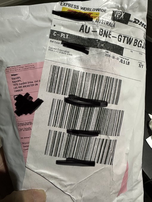 A hand holding a damaged shipping label from DHL Express Worldwide showing destination 'AU-BNE-GTWBGJ' (Australia - Brisbane) with barcodes and shipping information partially redacted with black marker.