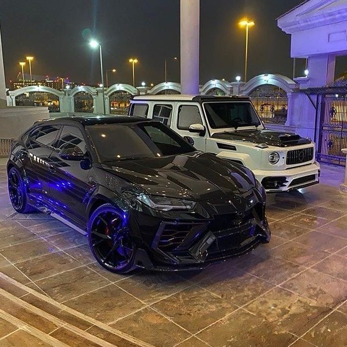 A black Lamborghini Urus parked at night next to a white Mercedes G-Wagon, both featuring custom modifications.