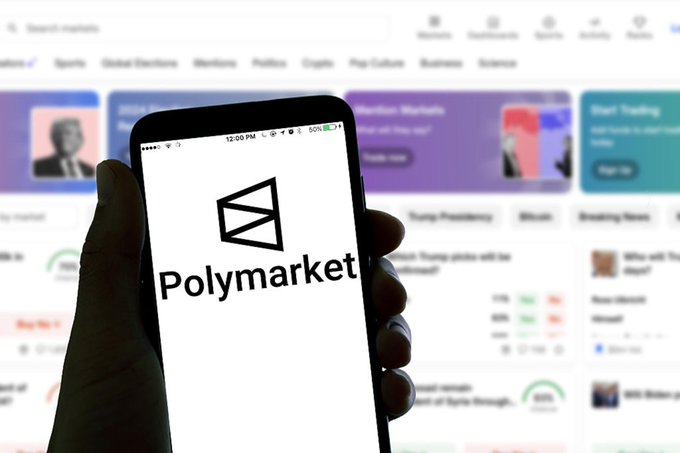 A hand holds a smartphone displaying the "Polymarket" logo, with the platform's website visible in the blurred background. The image relates to the post by illustrating the prediction platform where approximately $200 million in flagged suspicious trades occurred during the first half of 2026, driven largely by geopolitical and war-related bets.