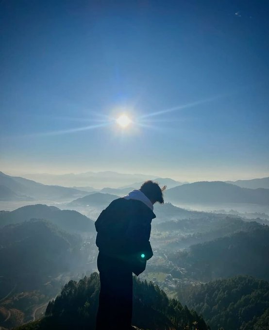 A silhouette of a person looking out over a misty mountain landscape at sunrise.