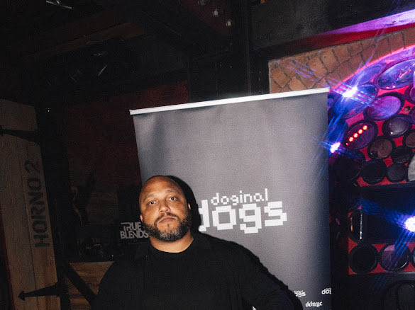 A man with a beard stands in front of a projection screen displaying "dosina 1095" at what appears to be an event or club setting.
