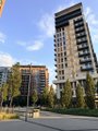 A tall building with a dark glass facade stands in the background of an outdoor urban setting with trees and a clear sky.