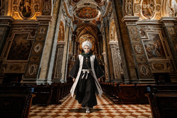 A cosplayer dressed as an anime character with white hair and a black and white robe stands in the aisle of an ornate cathedral.