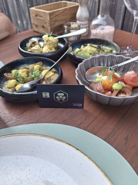 A restaurant table displays several small dishes of food including vegetables, bruschetta, and sides, with a 'VISA' card and an empty plate in the foreground.