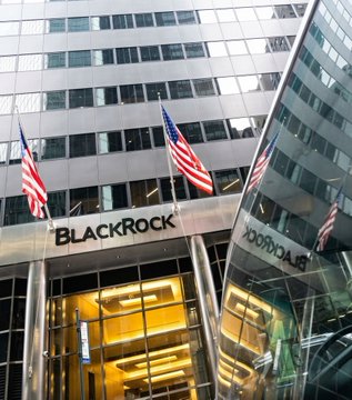 The image shows a large building with three American flags flying from its top, indicating that it might be located in an area where the United States has significant influence or importance. The building also displays the name "BlackRock" written in white letters on its facade. In the background, there is another building visible, but it does not have any text or flags displayed on it. The image seems to be related to a financial news article about Bitcoin Premium Income ETFs that has been posted for trading today.