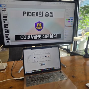 A workspace setup featuring a large monitor displaying a presentation slide titled 'PIDEX의 중심 COIX월렛 집중분석' alongside a laptop showing an Excel spreadsheet.