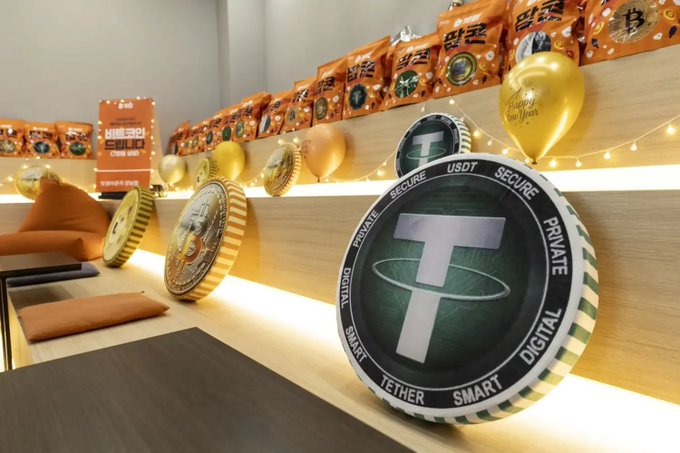 A 3D rendering of a brightly lit room decorated with crypto-themed items, prominently featuring a giant Tether (USDT) coin and other crypto coins, balloons, and shelves lined with snack packages.