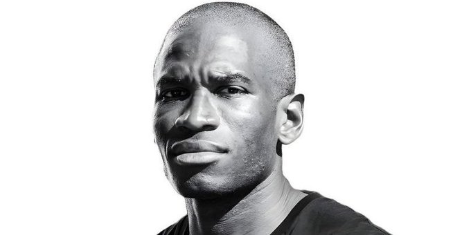 The image features a young man with a shaved head, wearing a black shirt against a white background. He appears serious as he gazes into the distance or looks at something above him, giving off an air of mystery or intensity. There are no texts in the image, and it seems to be a static visual display without any actions taking place. It is not clear what the post says, but the man's gaze and appearance suggest that he might be predicting some sort of event or news related to the current time period.