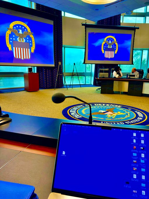 The photo captures a setup inside the U.S. Department of Defense, featuring the agency's official seal displayed on screens and a podium, alongside an open laptop showing a virtual desktop—likely taken by @3DOSNetwork during their participation in the live wargames alongside defense leaders like Boeing, Lockheed Martin, and Anduril.