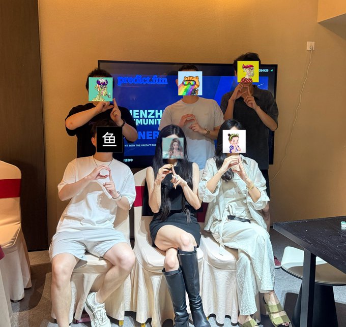 A group of six people posing at an event, holding up various NFT images over their faces, with a screen in the background displaying "predict.fun" and "SHENZHEN COMMUNITY WINNER."