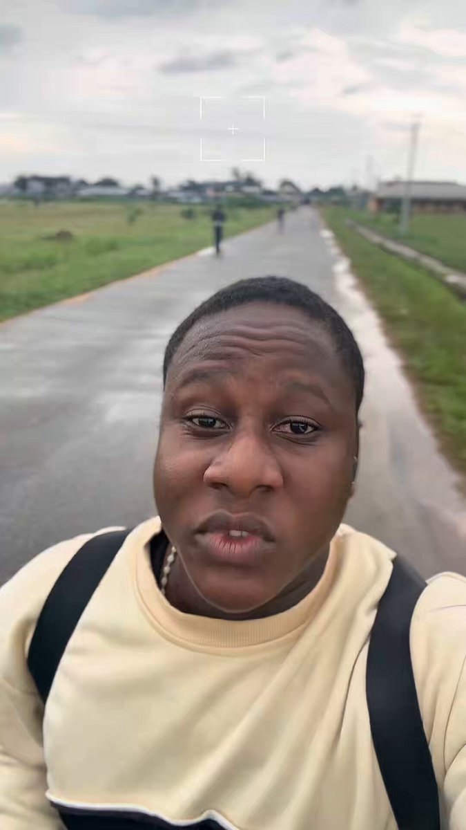 The image features a man wearing a yellow shirt standing on a road or path. He has a backpack on his back and appears to be posing for a picture with a serious expression, possibly indicating that he is taking part in an online challenge or participating in some sort of event related to the $Troll account. The post also mentions that there are people walking down the street nearby, which adds context to the location where the photo was taken.