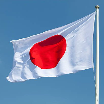The image features a Japanese flag flying high against a clear blue sky, with the word "Japan" written on it. Below the flag, there's a caption that reads "BREAKING Ripple launches RLUSD stablecoin in Japan." The text is positioned below the flag and slightly to the right of it.