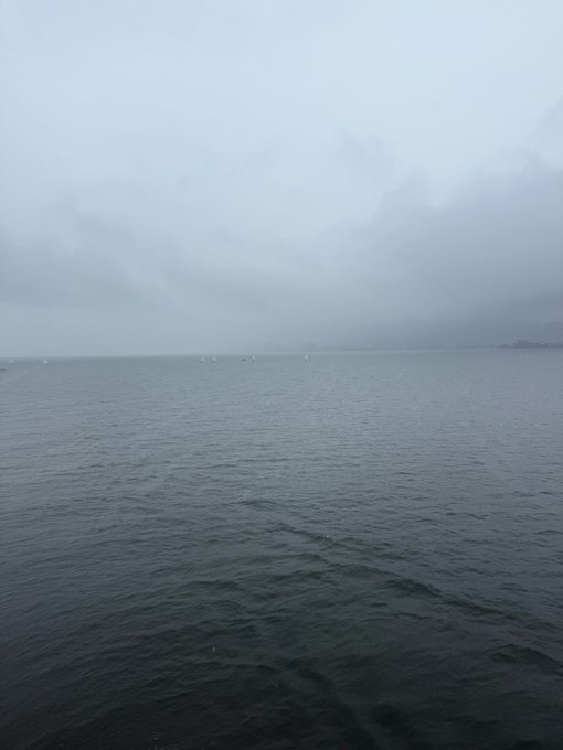 A misty, overcast seascape with calm grey water and distant fog-covered land.