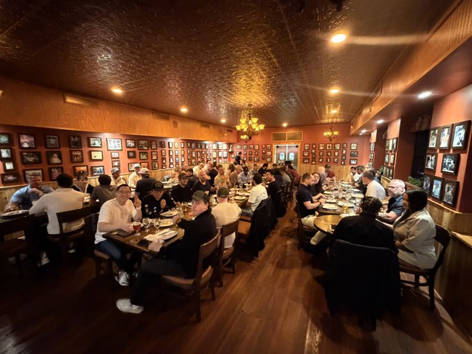 A crowded restaurant interior with warm lighting, a tin ceiling, and walls covered in framed photographs, filled with diners seated at tables.