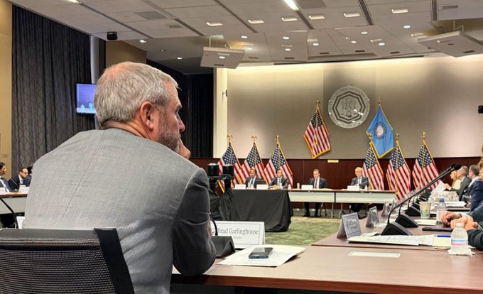 Brad Garlinghouse, identified by his name placard, is seen in attendance at what appears to be a formal government meeting, with American flags and a state seal visible in the background, suggesting his participation in discussions that align with his recent remarks about imminent U.S. crypto regulation.