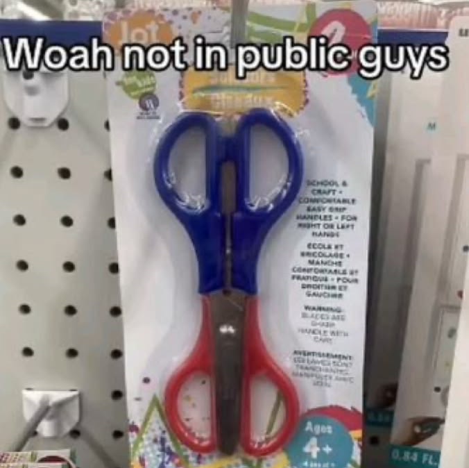 A package of children's scissors with blue and red handles designed for both right and left-handed use, labeled "Scissors" and "Ages 4+," is displayed on a store pegboard with the humorous caption "Woah not in public guys" overlaid on the image.
