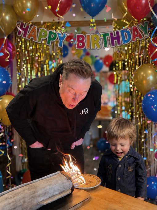 A man labeled with a "JR" monogram blows out candles on a small birthday cake alongside a young boy, with a "HAPPY BIRTHDAY" banner and colorful balloons decorating the festive scene.