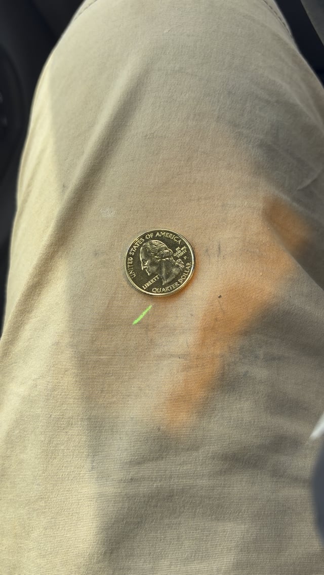 A 2020 United States of America quarter dollar coin (showing George Washington's profile) placed on light-colored fabric for size reference, with a green mark on the fabric beneath it.