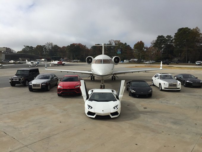 A private jet is parked on a tarmac, surrounded by a luxury fleet of vehicles including a white Lamborghini, black Rolls-Royce, red Lamborghini Urus, white Rolls-Royce, and other high-end cars, suggesting an exclusive gathering. The post "GM CT Me and my clients soon" implies an upcoming business event or showcase hosted by a General Motors representative in Connecticut.