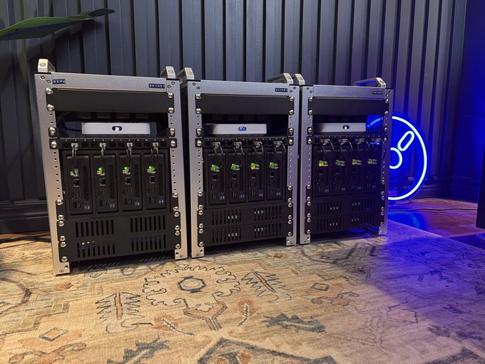 Three industrial server racks with cooling fans displayed on a patterned rug, with a blue neon lightsaber-style light in the background.