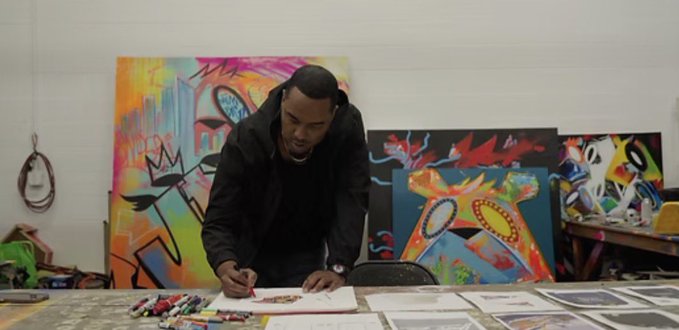 Artist Kingsaladeen signs his work in a studio surrounded by vibrant, graffiti-style paintings, collaborating with Yuga Labs on a new Bored Ape Yacht Club collection that captures the bold, expressive energy seen in his colorful artwork.