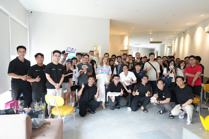 A diverse group of approximately 40-50 people gather indoors for a group photo, with some holding signs that appear to reference "Pudgy Penguins" and "Renaissance" branding. The caption "Asia Community Power, @pudgypenguins x @renaissCLTB" suggests this is a community meetup event bringing together members of these two blockchain/Web3 projects.