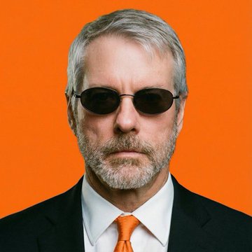 This image features Michael Saylor in a suit and sunglasses against an orange background, likely representing his call for the US Senate to approve the Crypto Clarity Act.