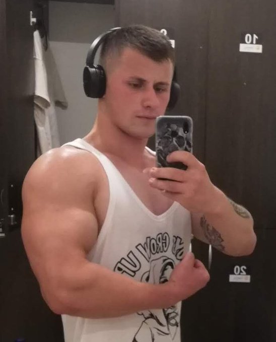 A muscular young man wearing a white tank top and over-ear headphones takes a mirror selfie in a locker room with stalls numbered "10" and "20" visible behind him, while his post encourages followers to support his rise to the TOP 100 on the @quipnetwork mindshare platform, where he's currently ranked #106.