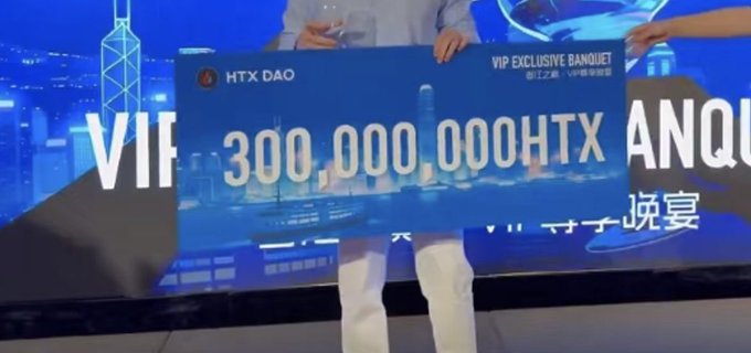 Two people hold up a large novelty check from HTX DAO for '300,000,000HTX' at what appears to be a VIP Exclusive Banquet event.