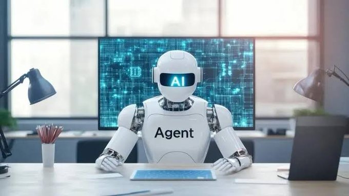 A white humanoid robot labeled "Agent" with "AI" on its screen display sits at a desk in an office setting with a monitor showing digital patterns behind it.