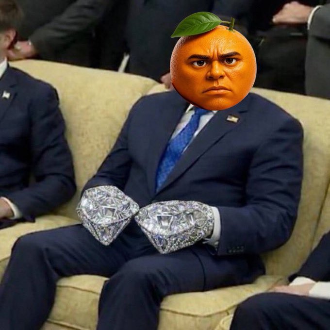 A meme image featuring a man in a dark suit with an orange fruit (with a leaf) replacing his head, with two large diamond graphics placed over his hands in his lap.
