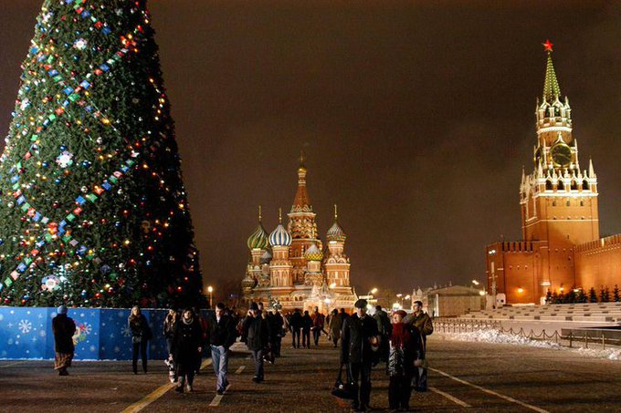A festive nighttime scene at Moscow's Red Square, featuring the iconic St. Basil's Cathedral with its colorful onion domes in the center, the Kremlin's Spasskaya Tower topped with a red star on the right, and a towering Christmas tree adorned with lights on the left, while visitors walk across the snow-dusted plaza—all tying into the post's reference to Russian Christmas (January 7 on the Julian Calendar) and its "bear" market hint at Russia, suggesting a holiday-themed bullish prediction for XRP.