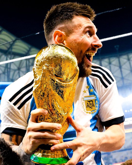 Lionel Messi joyfully embraces the FIFA World Cup trophy while wearing Argentina's iconic blue and white striped jersey featuring the AFA crest, his ecstatic expression capturing the culmination of his legendary international career highlighted in the post.