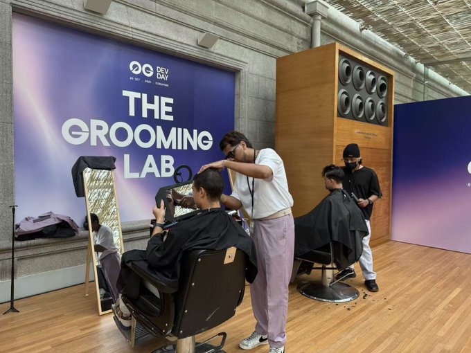 A promotional event for 'DEV DAY' titled 'THE GROOMING LAB' where barbers in white tees and lavender pants are giving haircuts to clients seated in barber chairs.