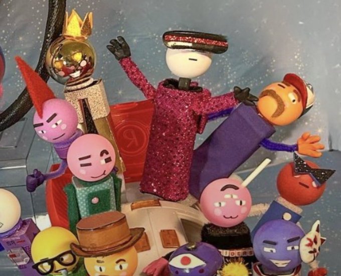 A collection of small claymation figures with various colorful character faces and accessories (crowns, top hats, masks) set against a starry night background.