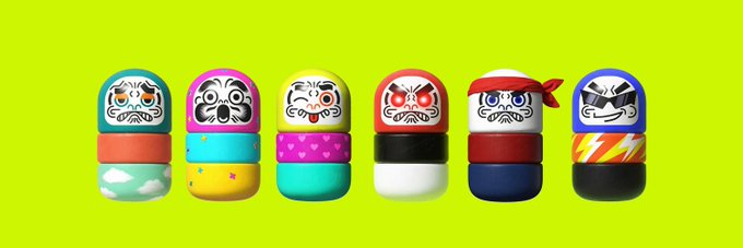 Six colorful Daruma dolls with various traditional Japanese opera mask designs on their faces are arranged in a row against a bright green background.