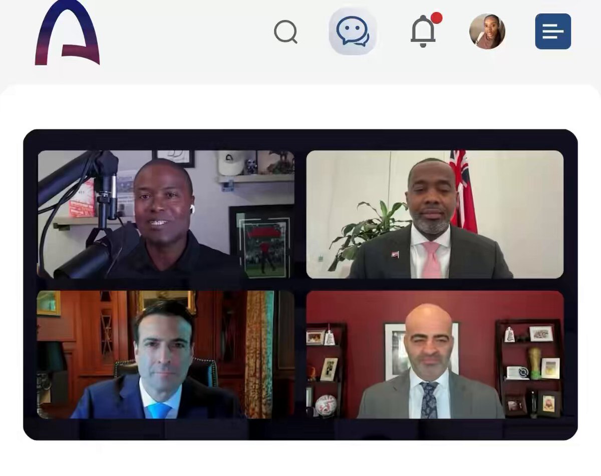 In this image, four men are sitting at a table for a video conference call. They appear to be engaged in a discussion or presentation related to Bermuda's economy. The screen displays their faces along with the names of the people involved in the conversation. The background shows a white wall and a potted plant, creating an office-like setting.