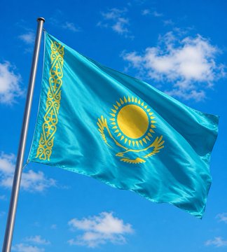 The flag of Kazakhstan waving against a bright blue sky with scattered white clouds, featuring its iconic turquoise background, golden sun with rays, and ornamental national pattern on the hoist side.