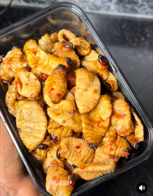 A plastic container filled with glazed, caramelized chicken wings or similar poultry pieces coated in a glossy sauce.