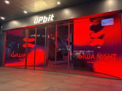 A storefront at night with red-lit windows displaying 'upbit' in white lettering on the left and 'GLOBAL NIGHT' on the right.