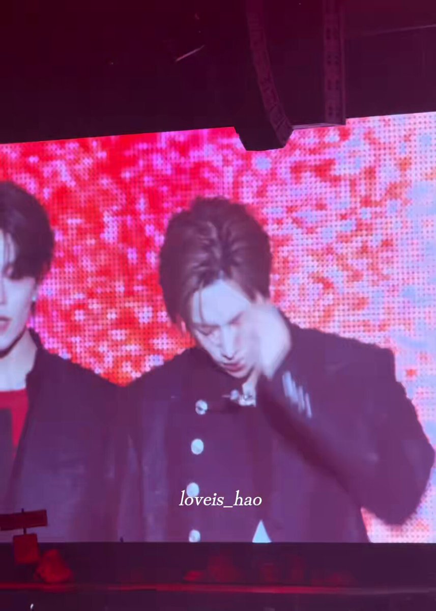 The image features a large screen with a man wearing a black suit, standing next to another person who has their arm around him. The background of the image is red, which appears to be part of an electronic display or projection system. There are also some words written in the image that read "loveis hao" and "#ARNO #아르노 가져온 파라이브원". The focus of this image is on the man wearing a black suit, standing next to another person who has their arm around him.