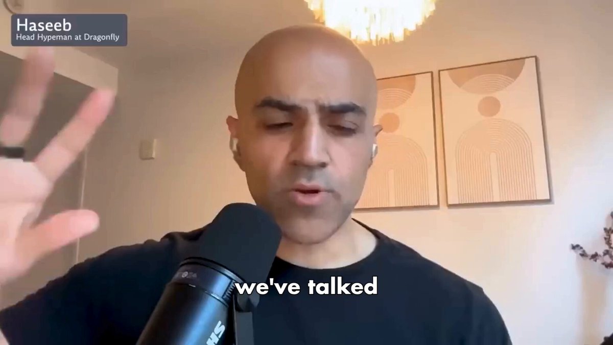 The image shows a man wearing a black shirt, standing in front of a microphone with his hands raised. The background features two pictures hanging on the wall behind him. The caption for the image reads "We've spoken", which suggests that they have just finished discussing something or sharing their thoughts and ideas.