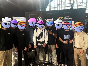 The image features a group of people posing for a photo, with each person wearing a hat or mask that resembles a character from a video game. The hats are predominantly pink and blue, adding a fun and playful element to the scene. One individual is holding up a sign that says "NFT Paris", possibly indicating an event or gathering related to the NFT industry.