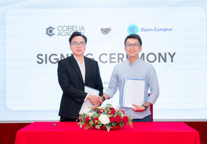 Two men in business attire shake hands and hold signed documents during a 'SIGNING CEREMONY' involving CORELIA ACADEMY and Open Campus.