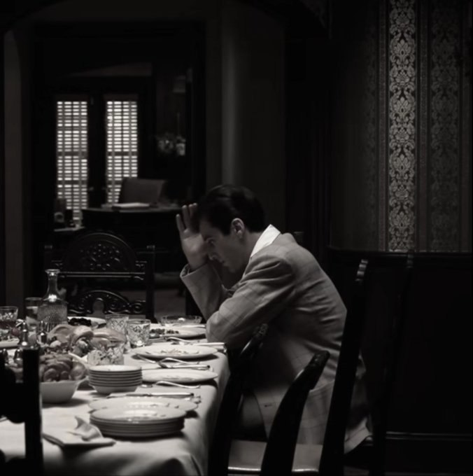 urns, bottles, and a vase are arranged on the table, with a man seated at a dining table in a dimly lit room.