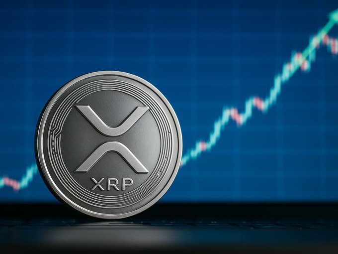 A silver XRP cryptocurrency coin sits in front of a blue background showing an upward-trending financial chart.