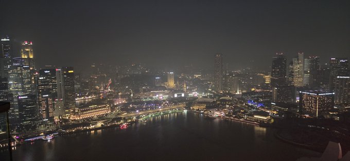 A nighttime aerial cityscape view of a river running through an urban area with illuminated skyscrapers, likely Singapore.