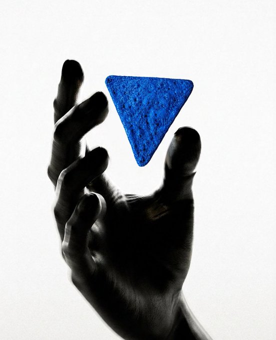 Artistic black and white photograph of a silhouetted hand holding up a vibrant blue triangular shape against a white background.